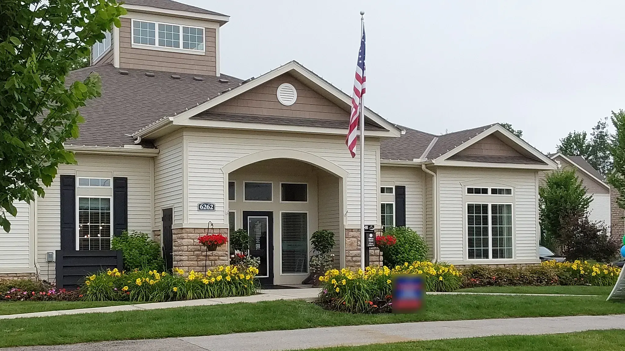 Apartment community clubhouse with an arched entry, flagpole and beds of yellow daylilies along the front walk