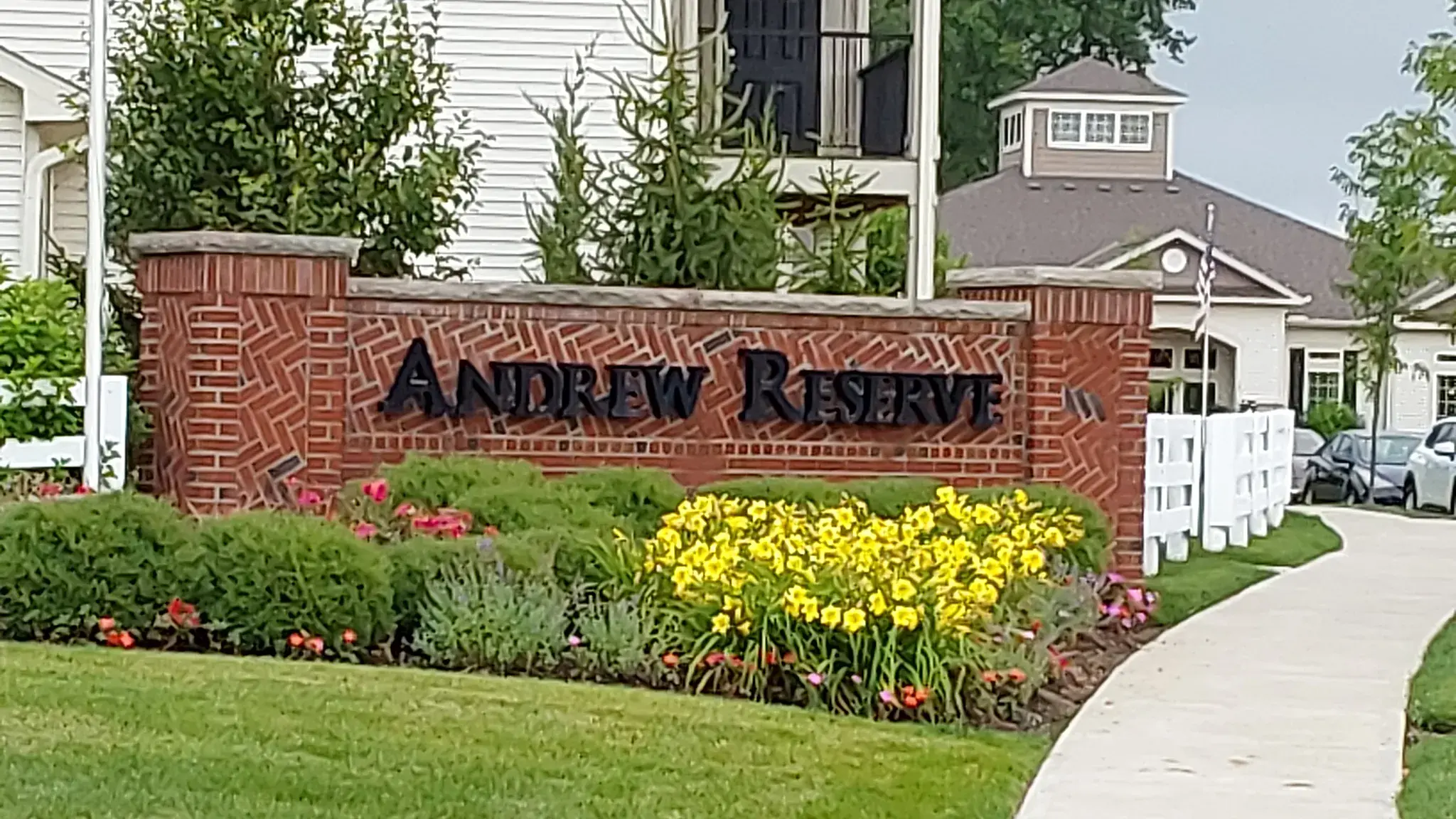 Brick apartment community entrance monument with a lush bed of yellow daylilies, clipped shrubs and annuals