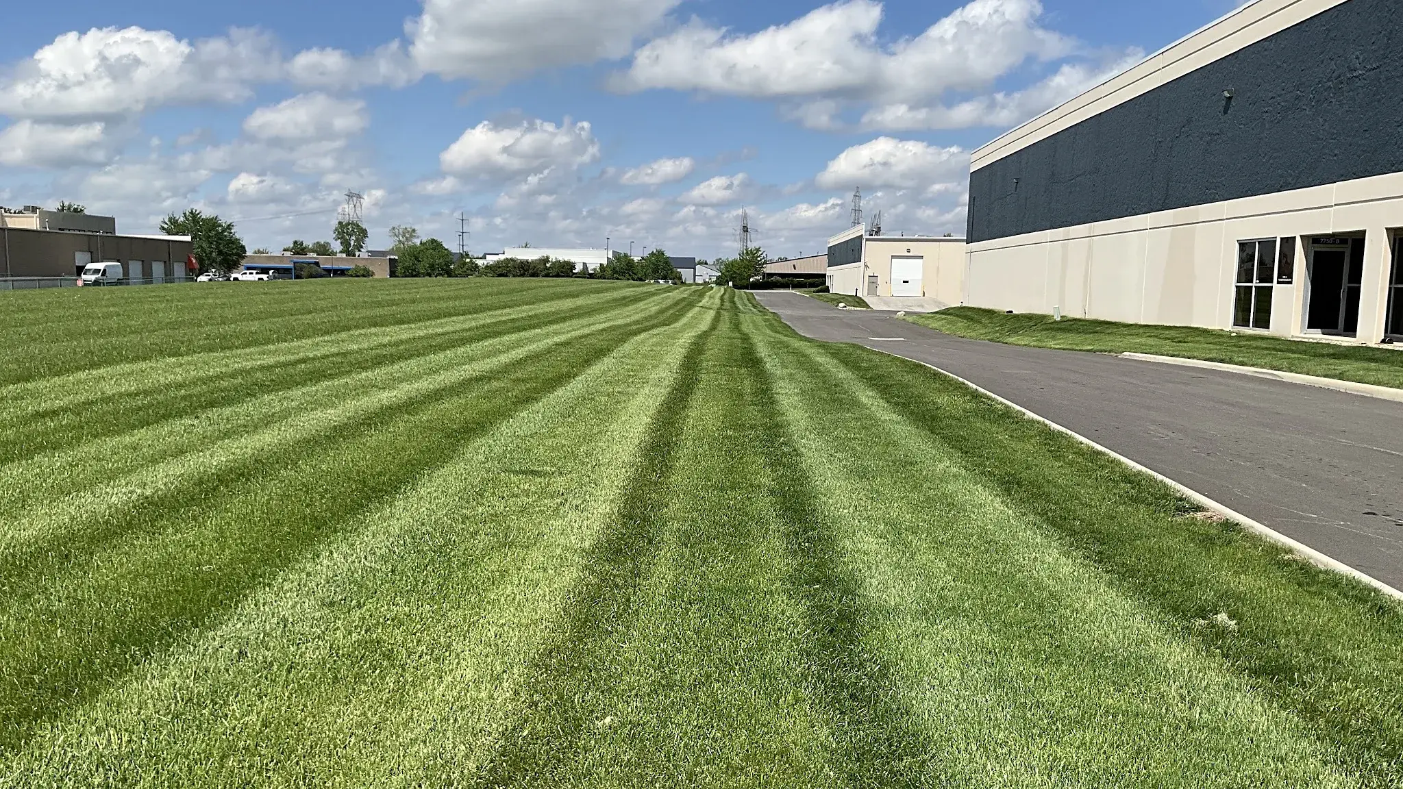 Crisp mowing stripes across a large lawn beside an industrial building at a commercial campus