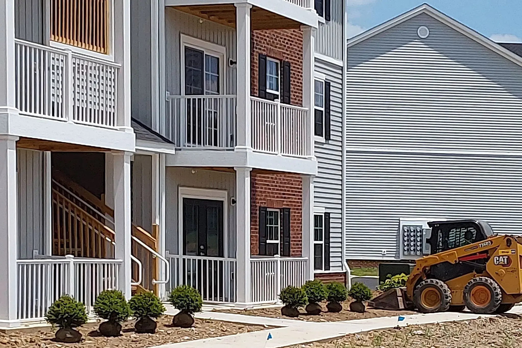 Newly planted boxwood foundation shrubs along the entry of a new apartment building with a skid steer on site