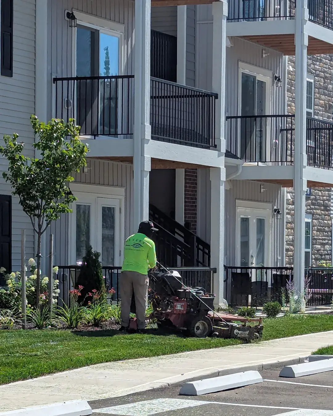 Crew member mowing the lawn with a walk-behind mower along the sidewalk at an apartment community