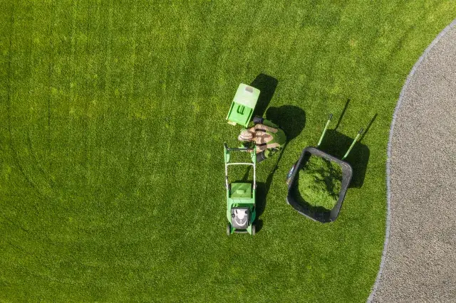 Overhead view of a freshly striped lawn with mower and clippings cart at work