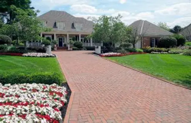 Herringbone brick paver driveway leading to an estate home with colorful annual flower beds