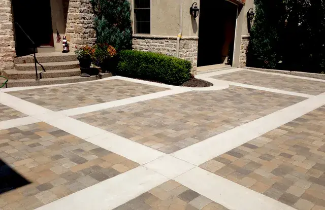 Multicolor paver driveway courtyard with contrasting concrete banding at a stone-front home