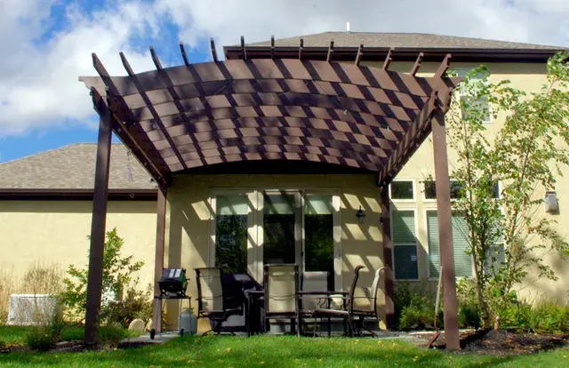 Arched timber pergola shading a backyard patio dining area behind a stucco home