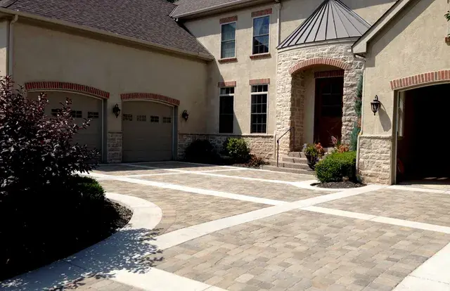 Paver motor court with white banding leading to garage doors and an arched stone entry