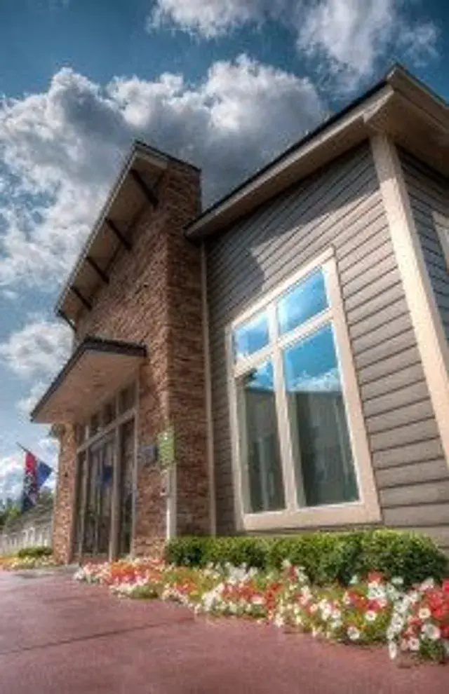 Leasing office entrance bordered by trimmed shrubs and colorful petunias along a red walkway