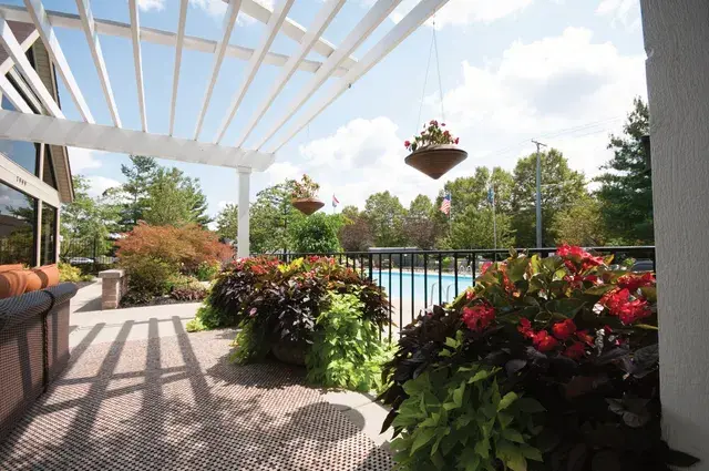White pergola walkway lined with tropical planters and hanging baskets beside a community pool