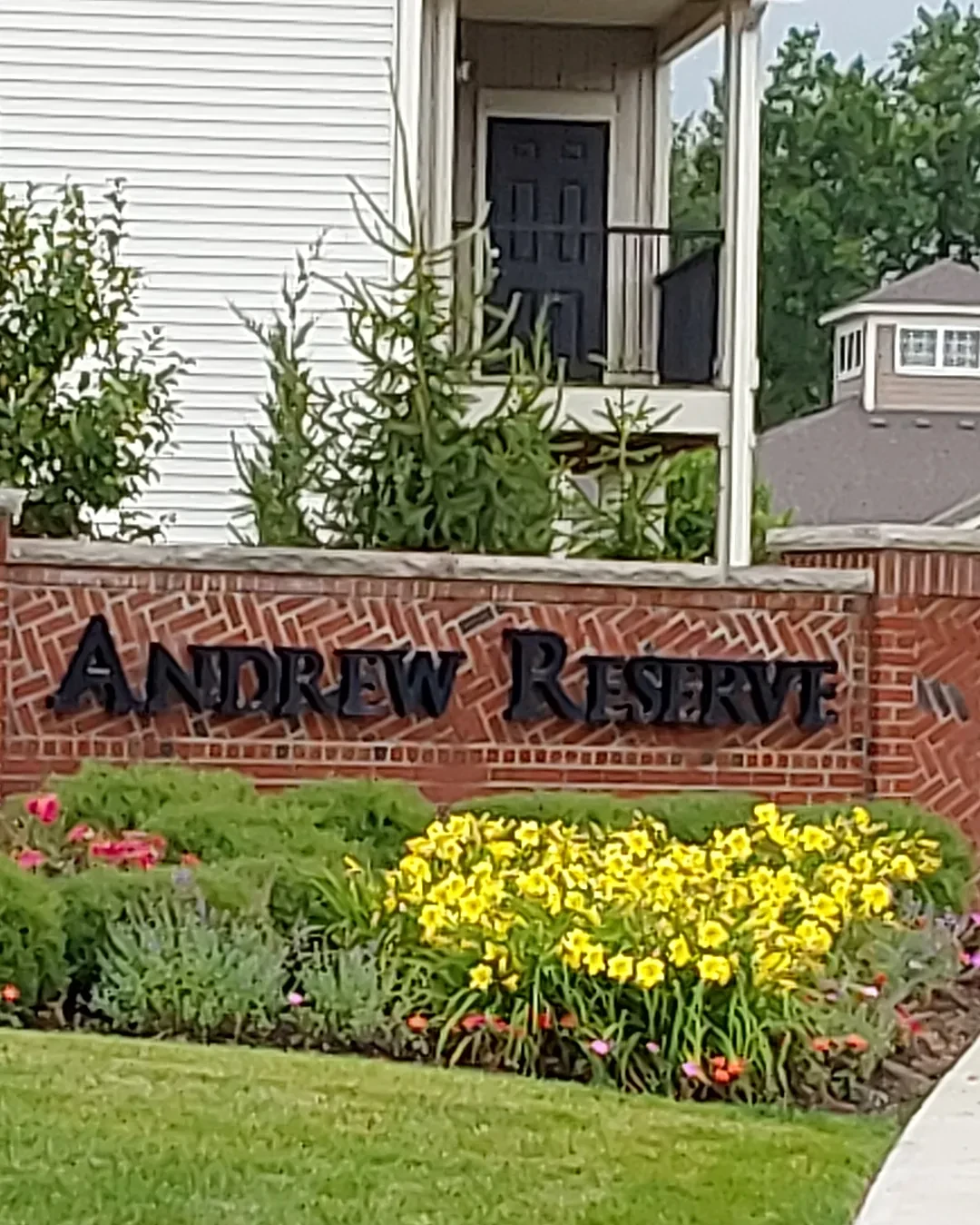 Brick apartment community entrance monument with a lush bed of yellow daylilies, clipped shrubs and annuals