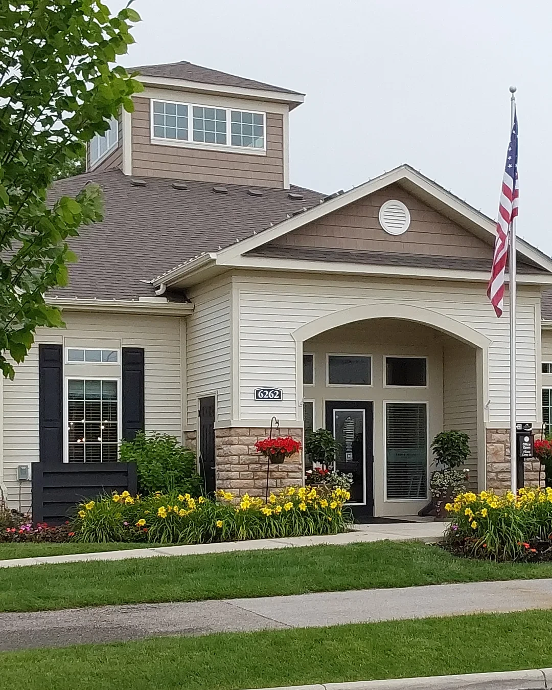 Apartment community clubhouse with an arched entry, flagpole and beds of yellow daylilies along the front walk