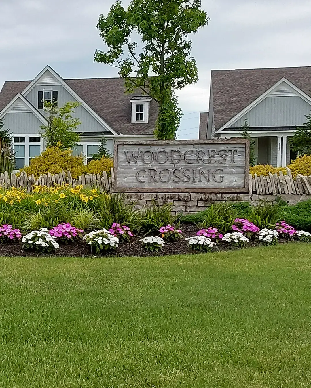 HOA community entrance with a stone pillar, rustic wood sign and a long bed of yellow daylilies and pink and white annuals