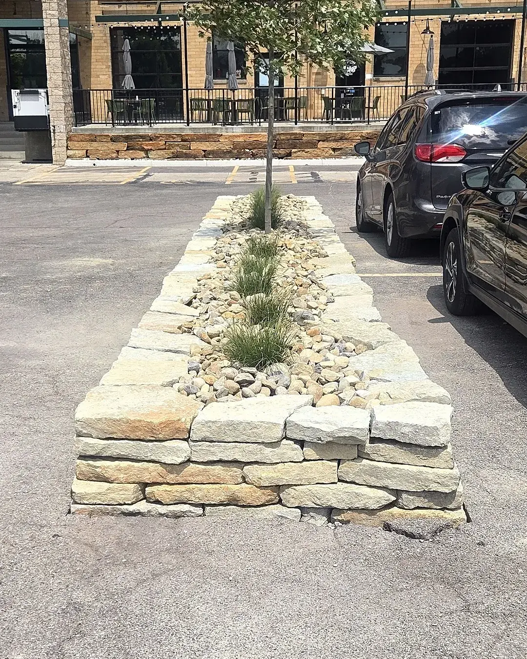 Newly built stone-edged landscape island with river rock and ornamental grasses in a commercial parking lot