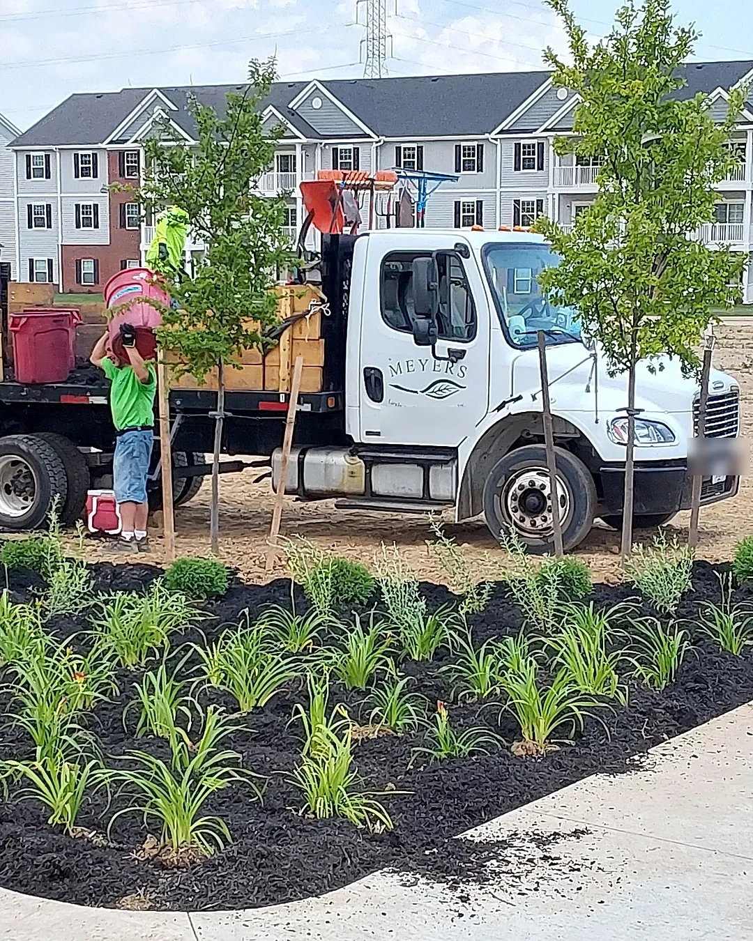 Meyers truck and crew planting a new daylily and shrub bed in fresh mulch at an apartment community under construction