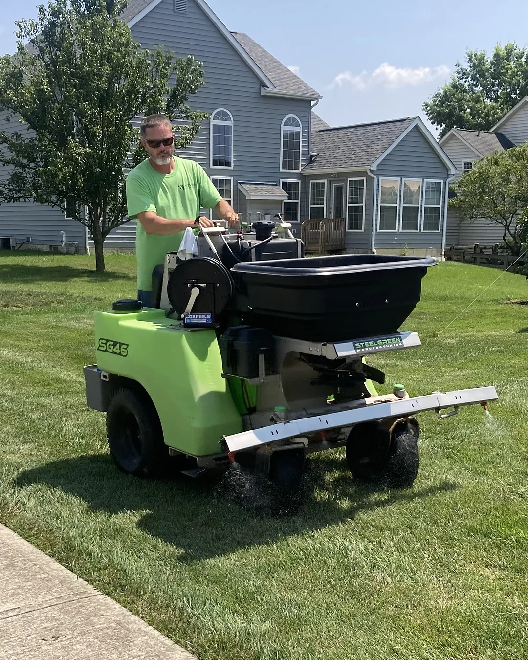 Lawn care technician applying a lawn treatment with a ride-on spreader across a mowed lawn